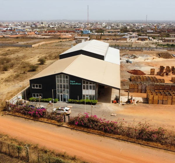 Vue aérienne des installations Agro Expedition Senegal à Diamniadio — bâtiment principal, abords végétalisés et zone de stockage extérieure